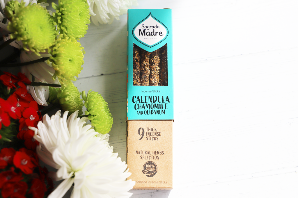 Sagrada Madre Calendula Chamomile and Olibanum incense pack on white background with colorful flowers next to it.