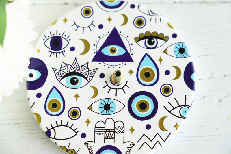 Decorative incense burner with geometric and eye patterns on a white surface.