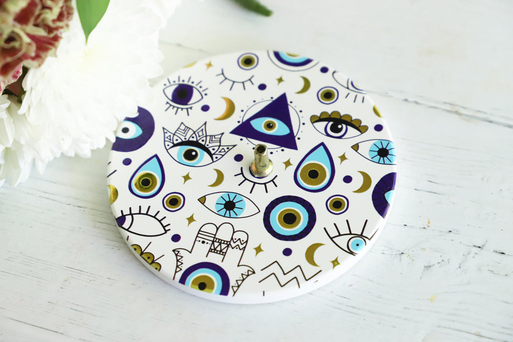 Decorative incense burner with geometric and eye patterns on a white surface.