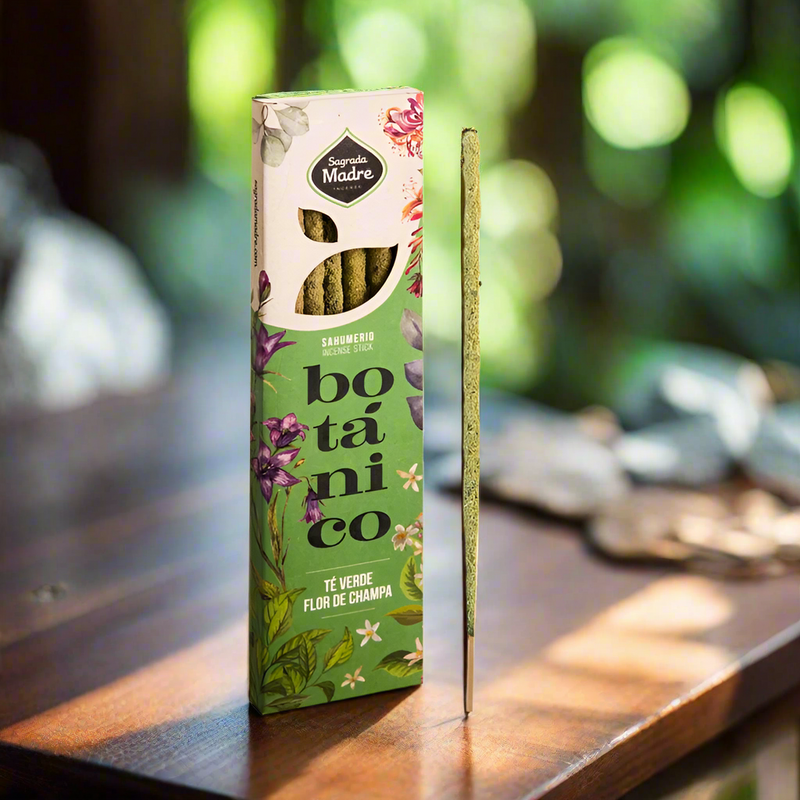 Sagrada Madre Green Tea and Champa incense package on a wooden table with blurry greenery in the background