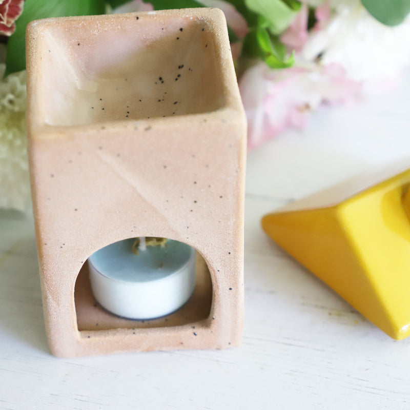 Decorative oil burner with a small candle inside, surrounded by flowers on a light surface.