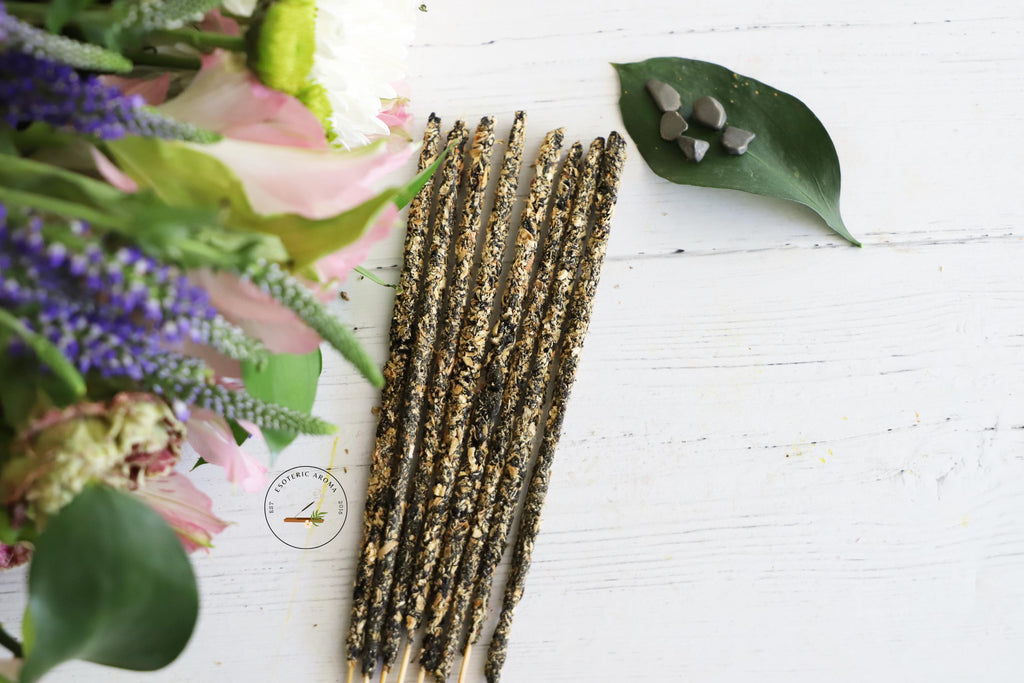 Incense stick bunch with a leaf and on the leaf are a few pyrite chips. On a white background with flowers