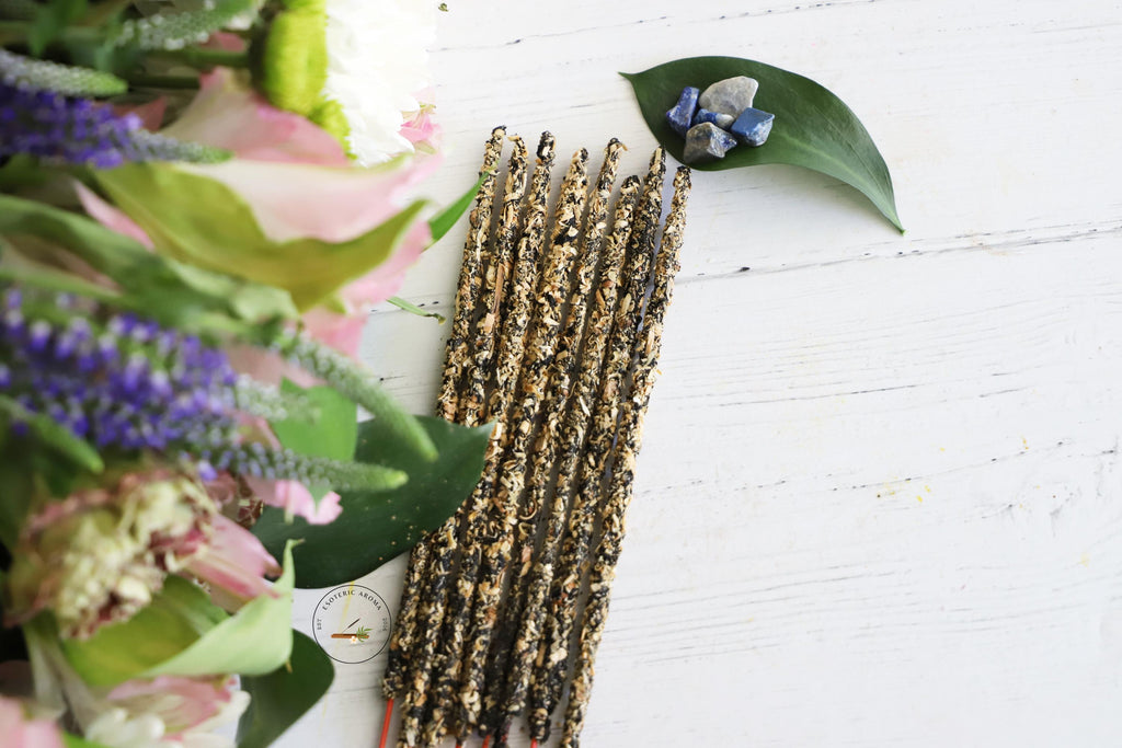 Incense bunch with a leaf next to it with Lapis Lazuli chips on top. On a white background and fresh flowers on the side.
