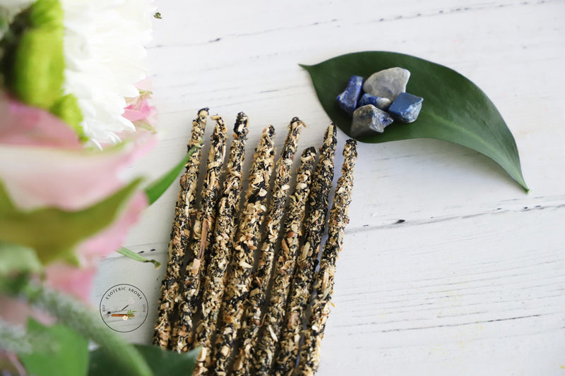 Incense bunch with a leaf next to it with Lapis Lazuli chips on top. On a white background and fresh flowers on the side.