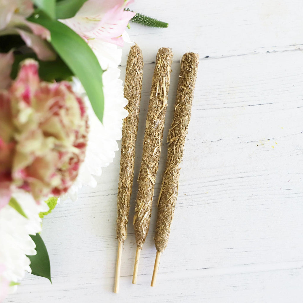 Three thick incense sticks on a white background with fresh flowers on the side.