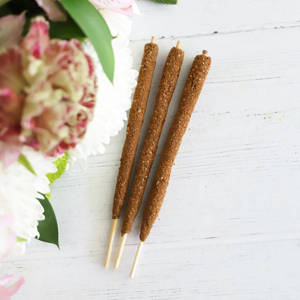 Three incense sticks on white background with fresh flowers on the side.