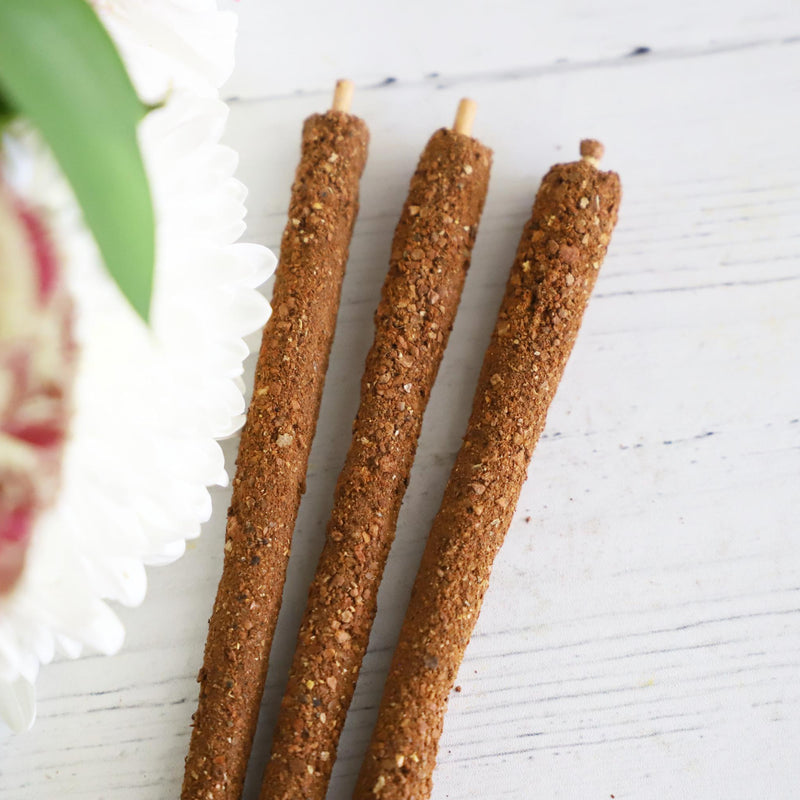 Three incense sticks on white background with fresh flowers on the side.
