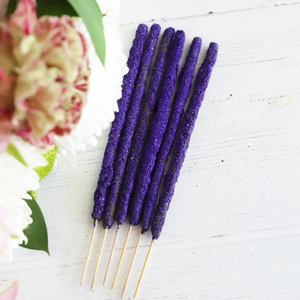Brightly colored incense sticks on a white background with fresh flowers on the side.