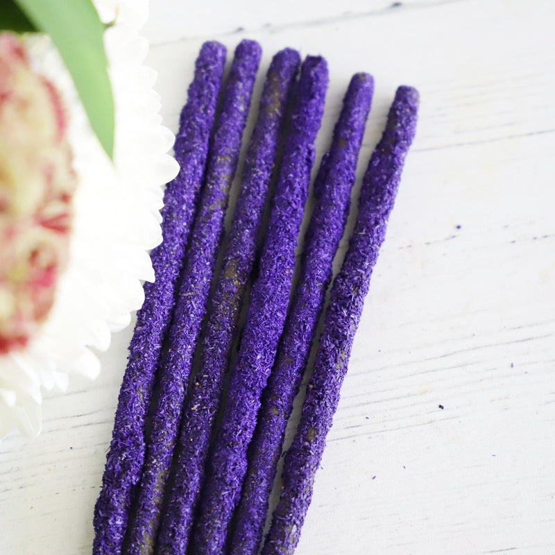 Brightly colored incense sticks on a white background with fresh flowers on the side.