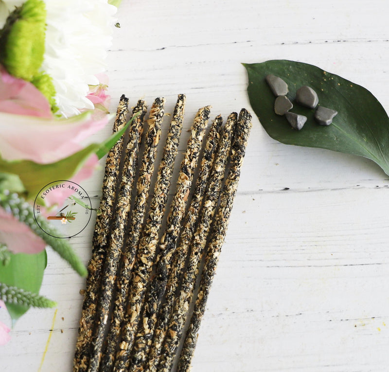 Incense stick bunch with a leaf and on the leaf are a few pyrite chips. On a white background with flowers