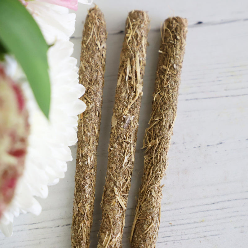Three thick incense sticks on a white background with fresh flowers on the side.