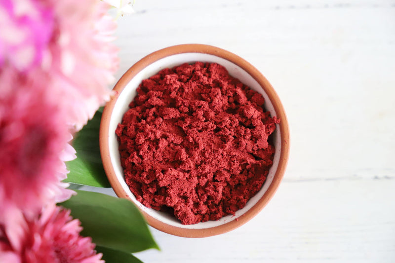 Red incense powder in a white bowl on white background with pink, red and green flowers.