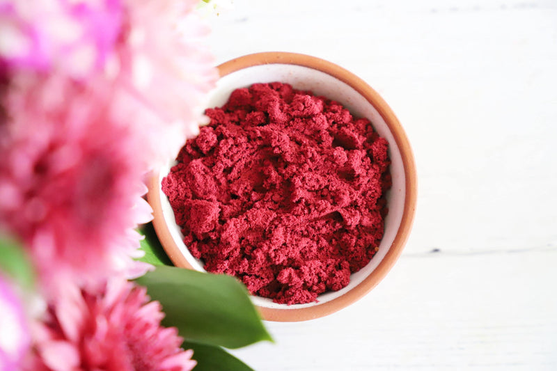 Red incense powder in a small bowl on a white background with colorful fresh flowers on the side.