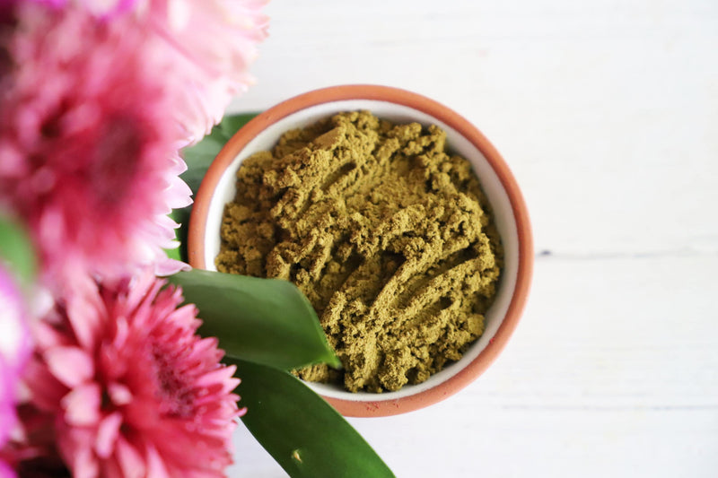 Incense powder in a small dish on a white background with colorful fresh flowers next to it.