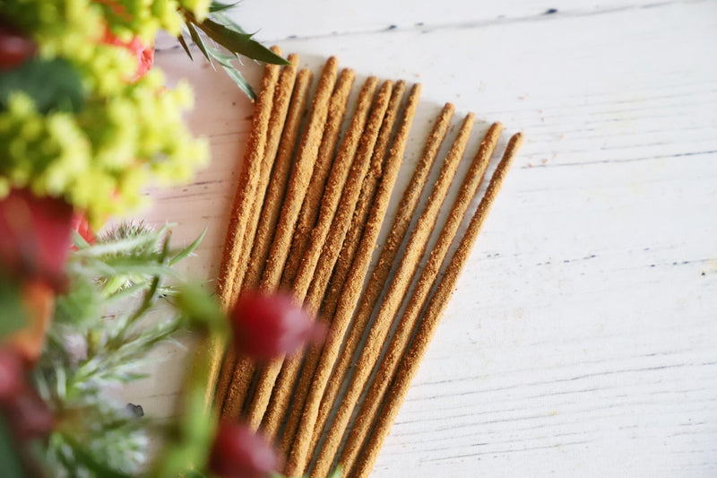 Incense sticks on white background with fresh red, yellow and green flowers next to them.