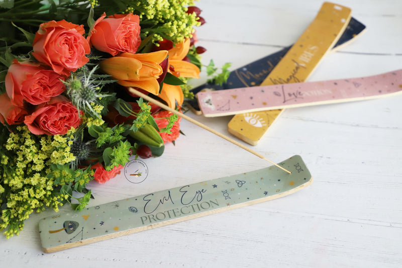 4 colorful celestial themed incense holders on white background with colorful fresh flowers next to them.