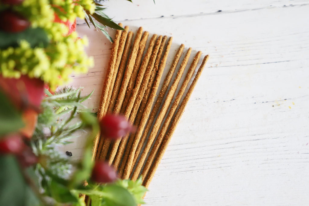 Incense sticks on white background with fresh red, yellow and green flowers next to them.
