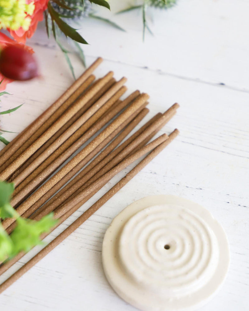 Incense sticks with round white incense holder on white background with colorful flowers next to them.