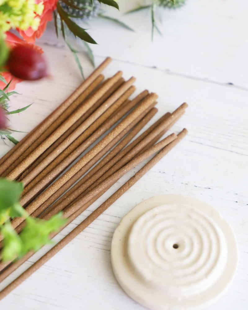 Incense sticks with round white incense holder on white background with colorful flowers next to them.
