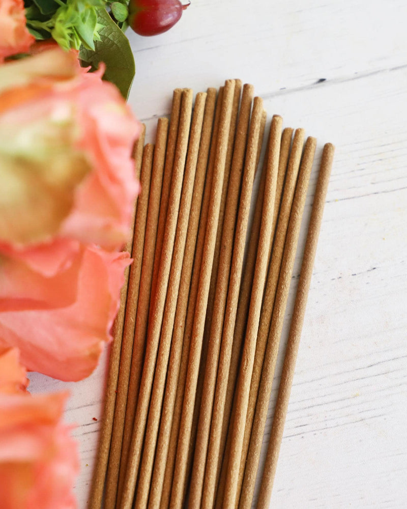 Incense sticks on white background with colorful fresh flowers next to them.