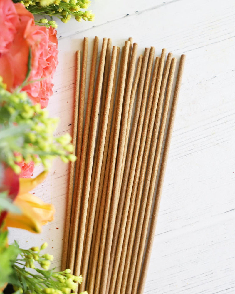 Incense sticks on white background with colorful flowers and greenery next to it.