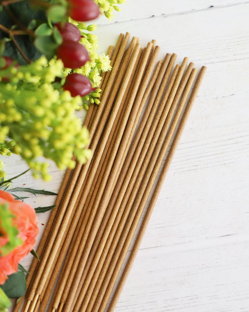 Incense sticks on white background with colorful fresh flowers and greenery next to it.