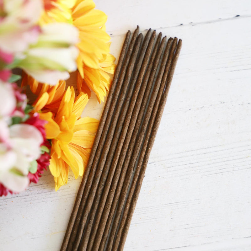 Incense sticks on a white background with bright, fresh flowers next to it.