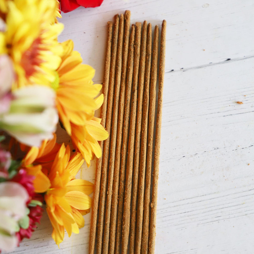 Incense sticks on white background with colorful fresh flowers next to them.