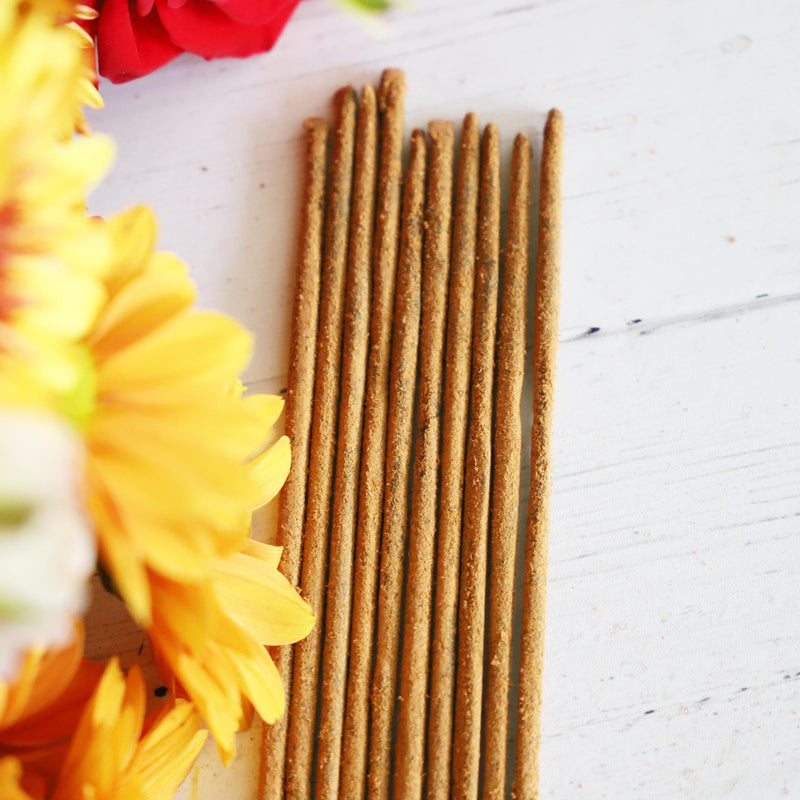 Incense sticks on white background with colorful fresh flowers next to them.