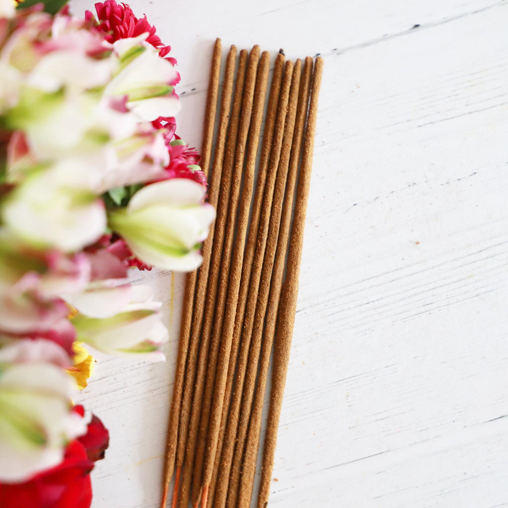 Incense sticks on a white background with colorful flowers next to them.