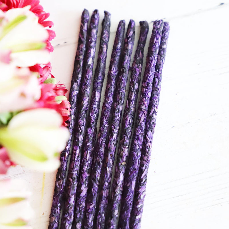 Purple incense sticks on white background with colorful flowers next to it.