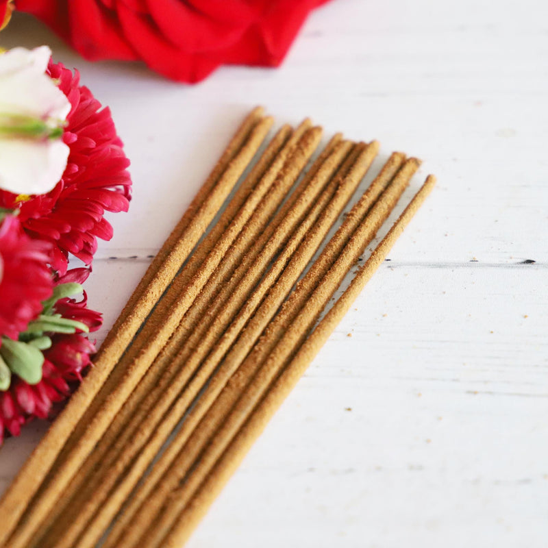 Incense stick bundle on white background with colorful fresh flowers next it.