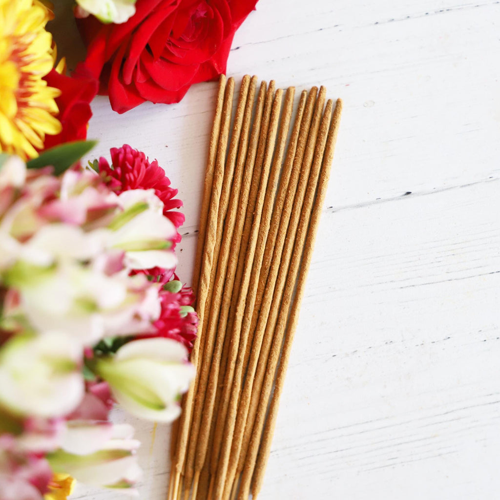 Incense stick bundle on white background with colorful fresh flowers next to it.