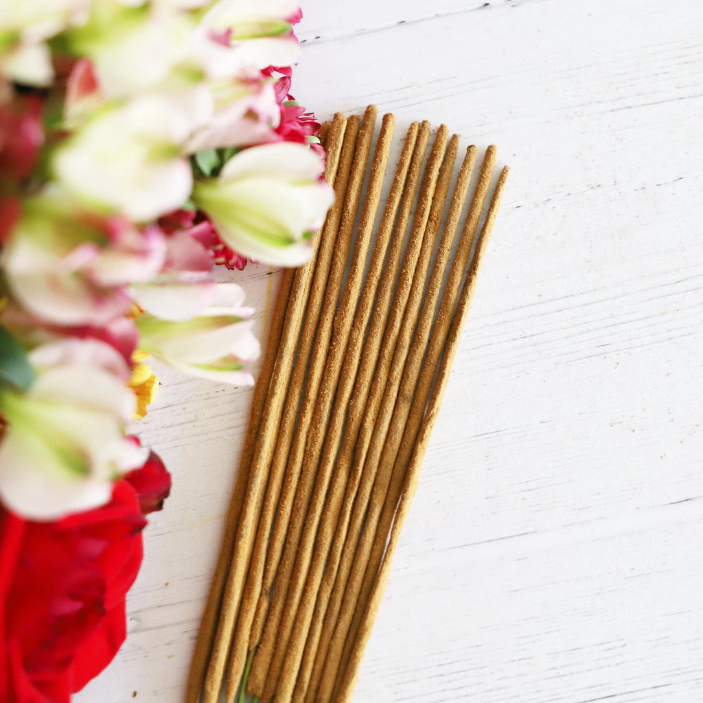 Incense sticks on a white background with colorful fresh flowers next to it.