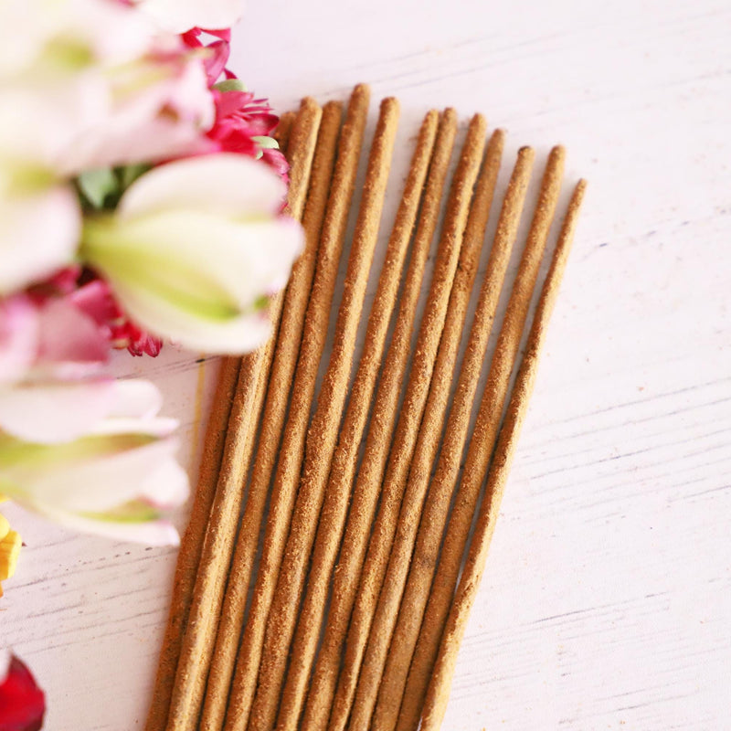 Incense sticks on a white background with colorful fresh flowers next to it.