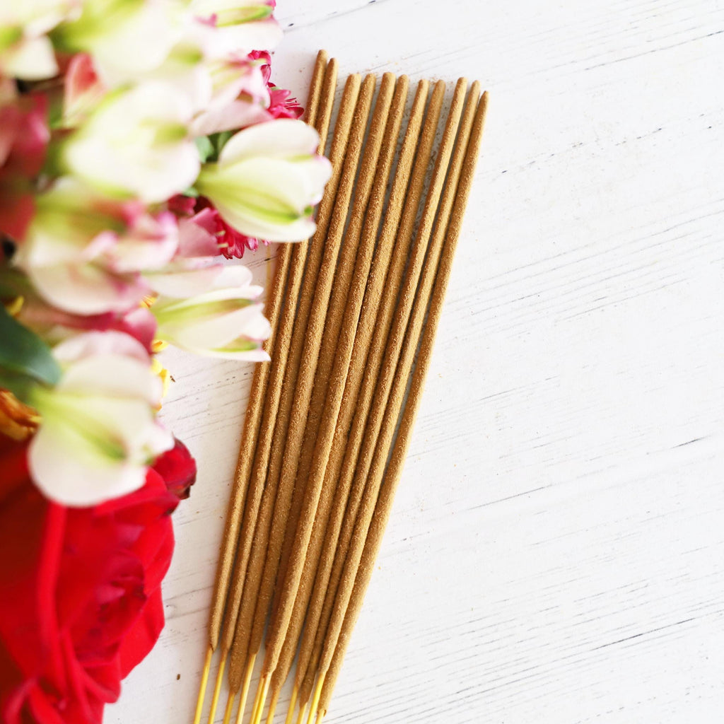 Incense sticks on a white background with colorful flowers next to it.