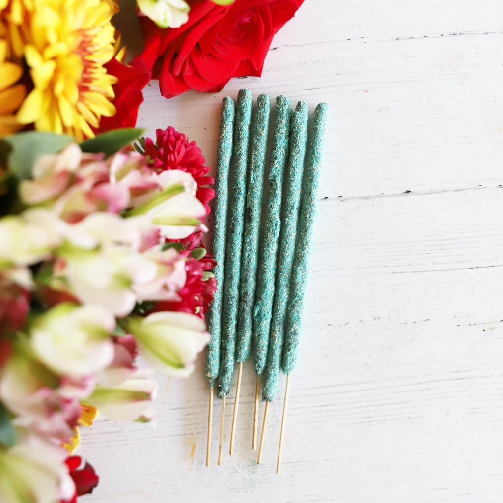 Blue green incense sticks on white background with colorful fresh flowers next to it.