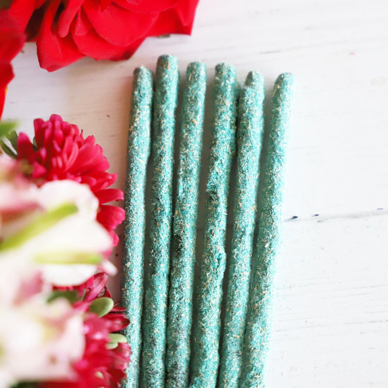 Blue green incense sticks on white background with colorful fresh flowers next to it.