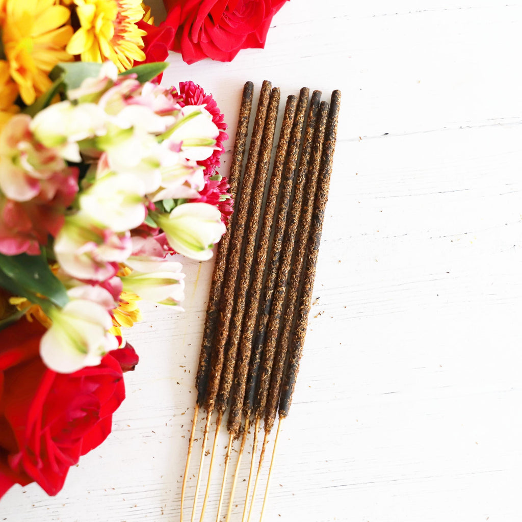 Incense stick bundle on a white background with red, white, yellow and green flowers next to it.