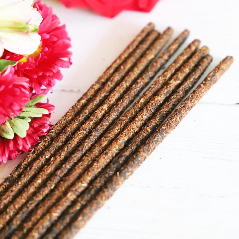 Incense sticks on white background next to pink, white and green flowers.
