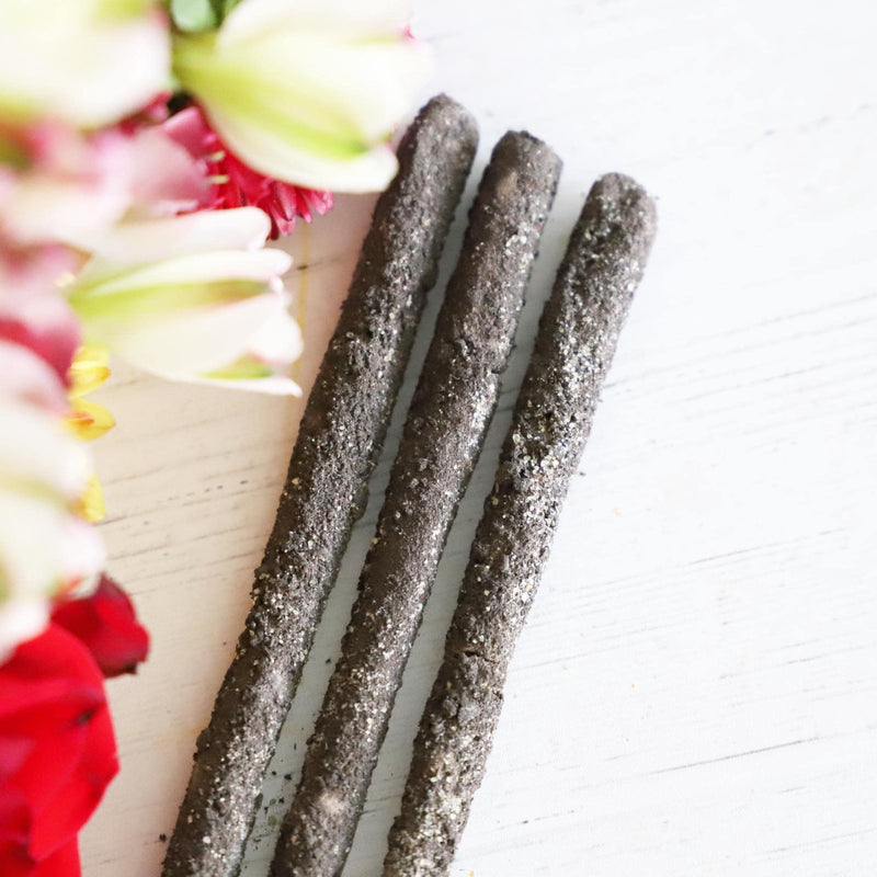 Three incense sticks on a white background with red, yellow and white flowers next to them.
