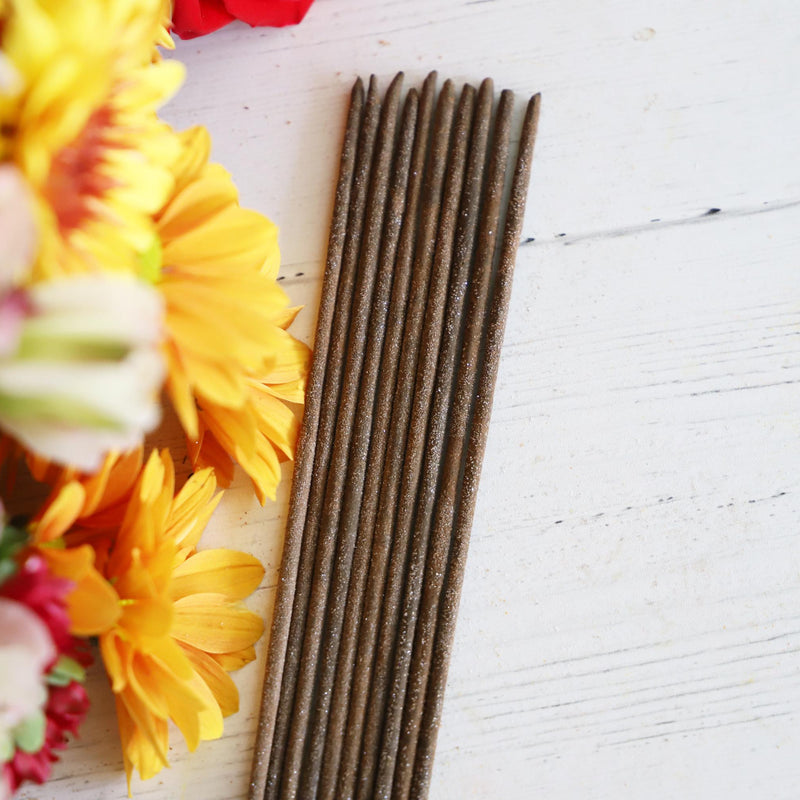 Bundle of incense sticks on a white background with colorful flowers next to it.