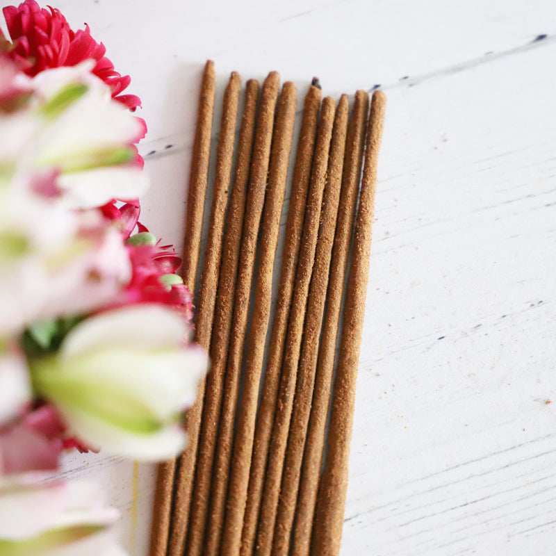 Incense sticks on a white background with colorful flowers next to them.