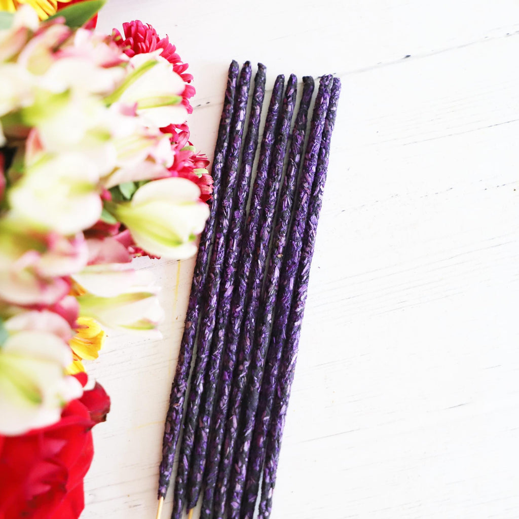 Purple incense sticks on white background with colorful flowers next to it.