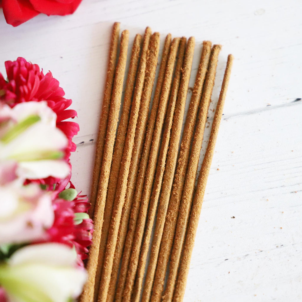 Incense stick bundle on white background with colorful fresh flowers next it.