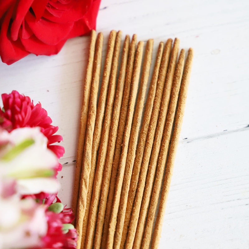 Incense stick bundle on white background with colorful fresh flowers next to it.