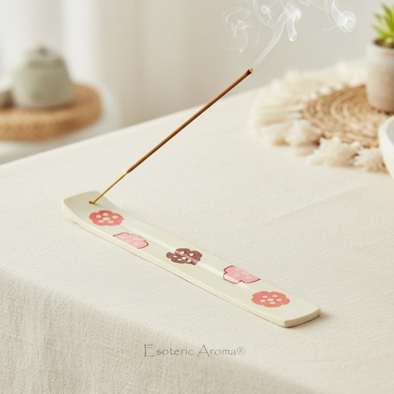 Floral incense burner with a lit incense in it on a linen cloth in a bright, boho room.