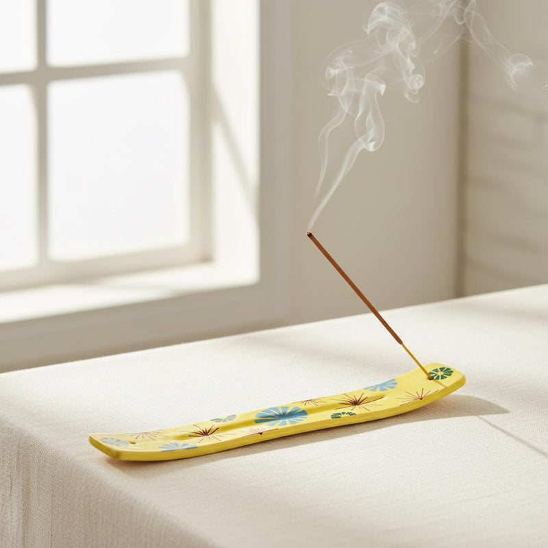 Yellow incense holder with a lit incense stick in it, smoke curling, a window in the background in a peaceful room