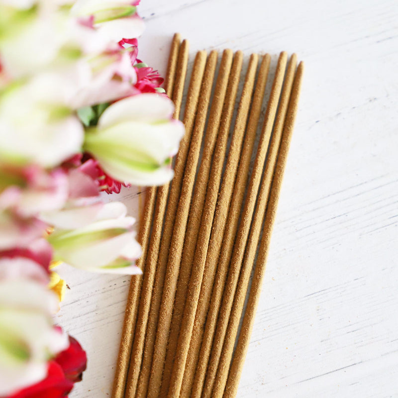 Incense sticks on a white background with colorful flowers next to it.