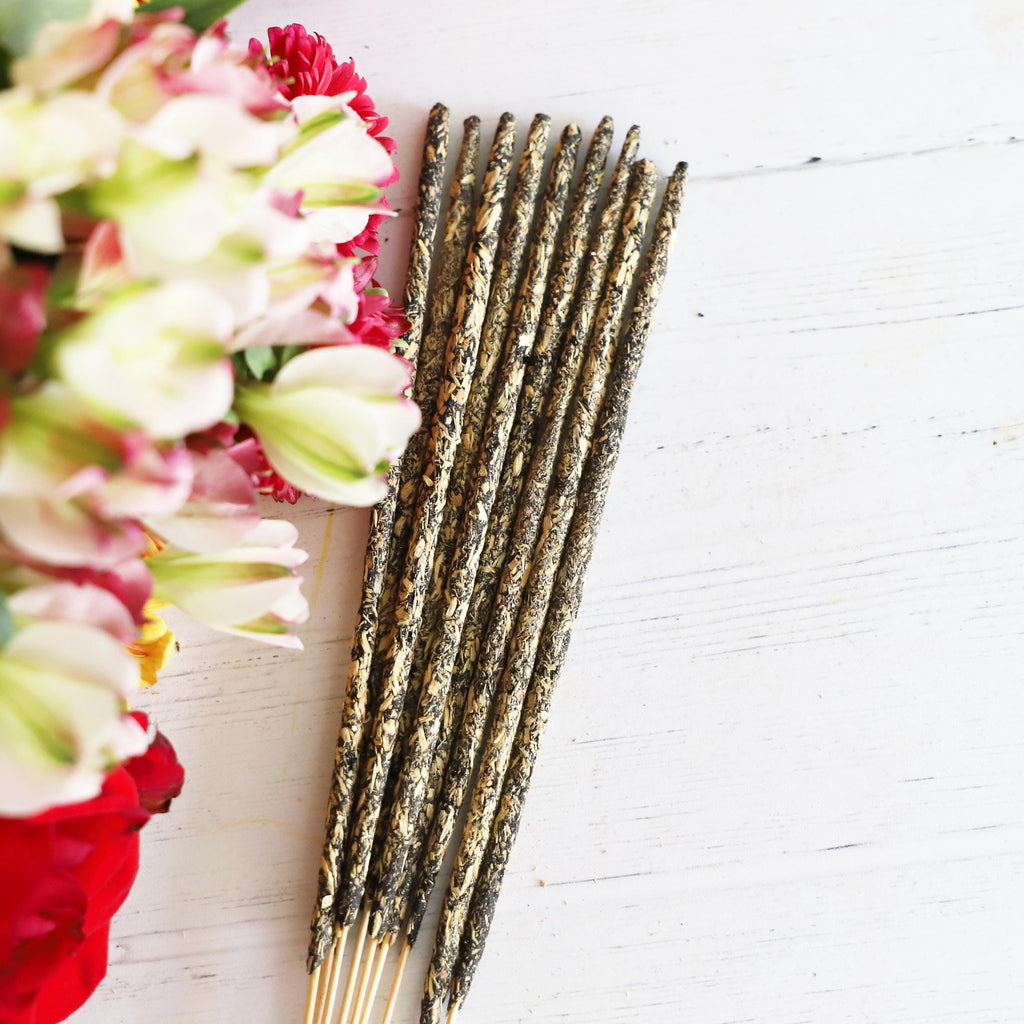 Incense sticks on white background with red and white fresh flowers next to it.